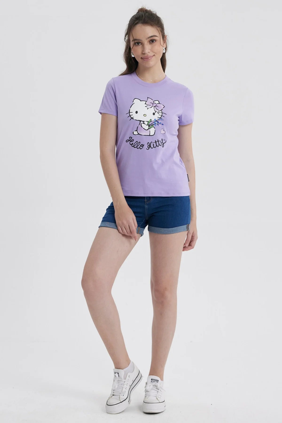 Polera lila de algodón con ilustración de Hello Kitty sosteniendo flores, diseño minimalista en el centro y texto 'Hello Kitty' en negro.