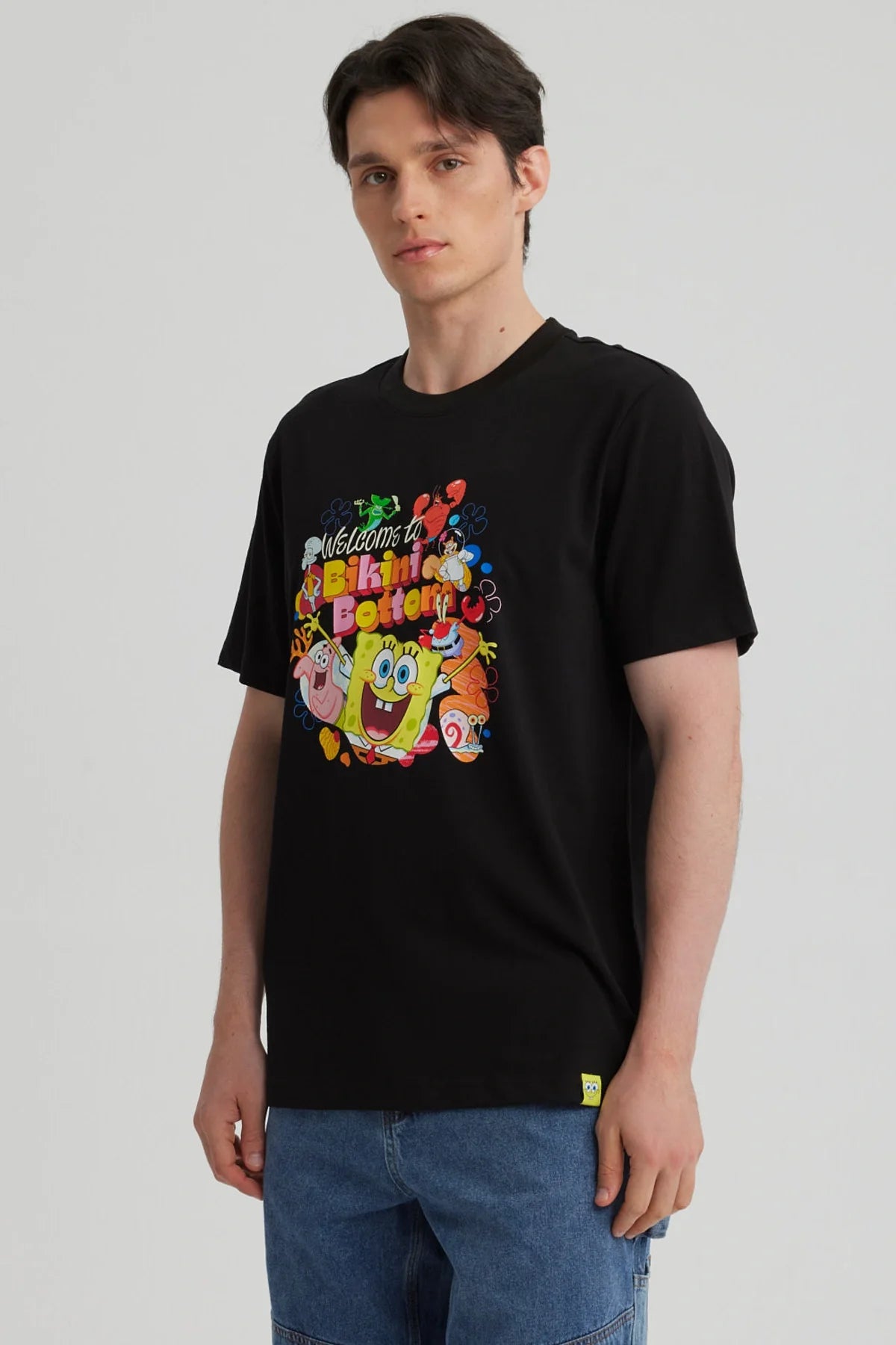 Polera negra de algodón con estampado colorido de Bob Esponja y amigos, mostrando la frase 'Welcome to Bikini Bottom' en un diseño vibrante y divertido.