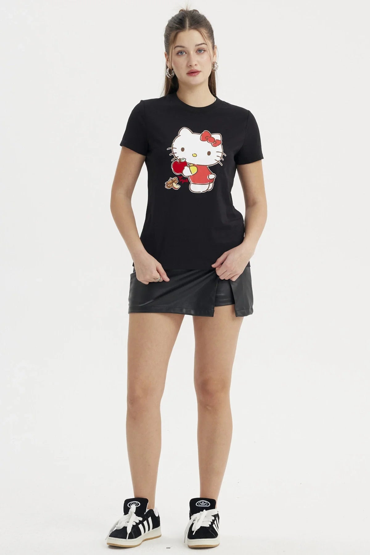 Polera negra de algodón con un diseño colorido de Hello Kitty sosteniendo una manzana roja, con un estilo kawaii que resalta su ternura icónica.