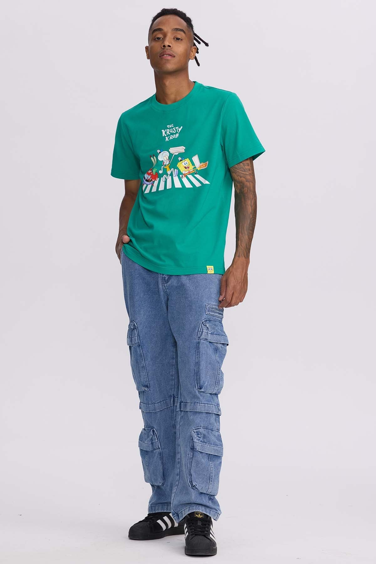 Polera verde con estampado de los personajes Bob Esponja, Calamardo y Don Cangrejo en la famosa escena de cruce peatonal, representando el Krusty Krab.