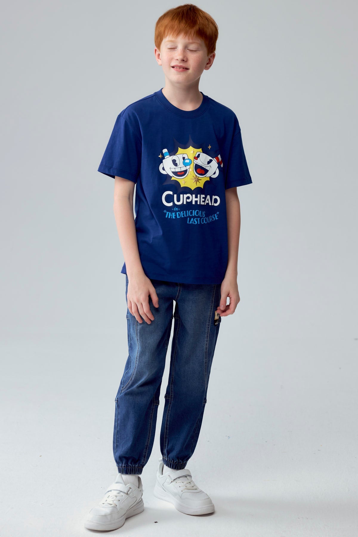 Polera azul de Cuphead con ilustración vibrante de Cuphead y Mugman sonriendo, destacando el título 'Cuphead in The Delicious Last Course' en un diseño retro.
