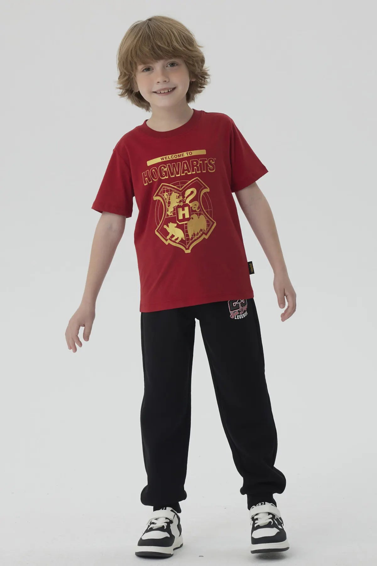Polera burdeos de algodón con el escudo de Hogwarts en dorado, destacando la frase 'WELCOME TO HOGWARTS', ideal para los pequeños magos fans de Harry Potter.