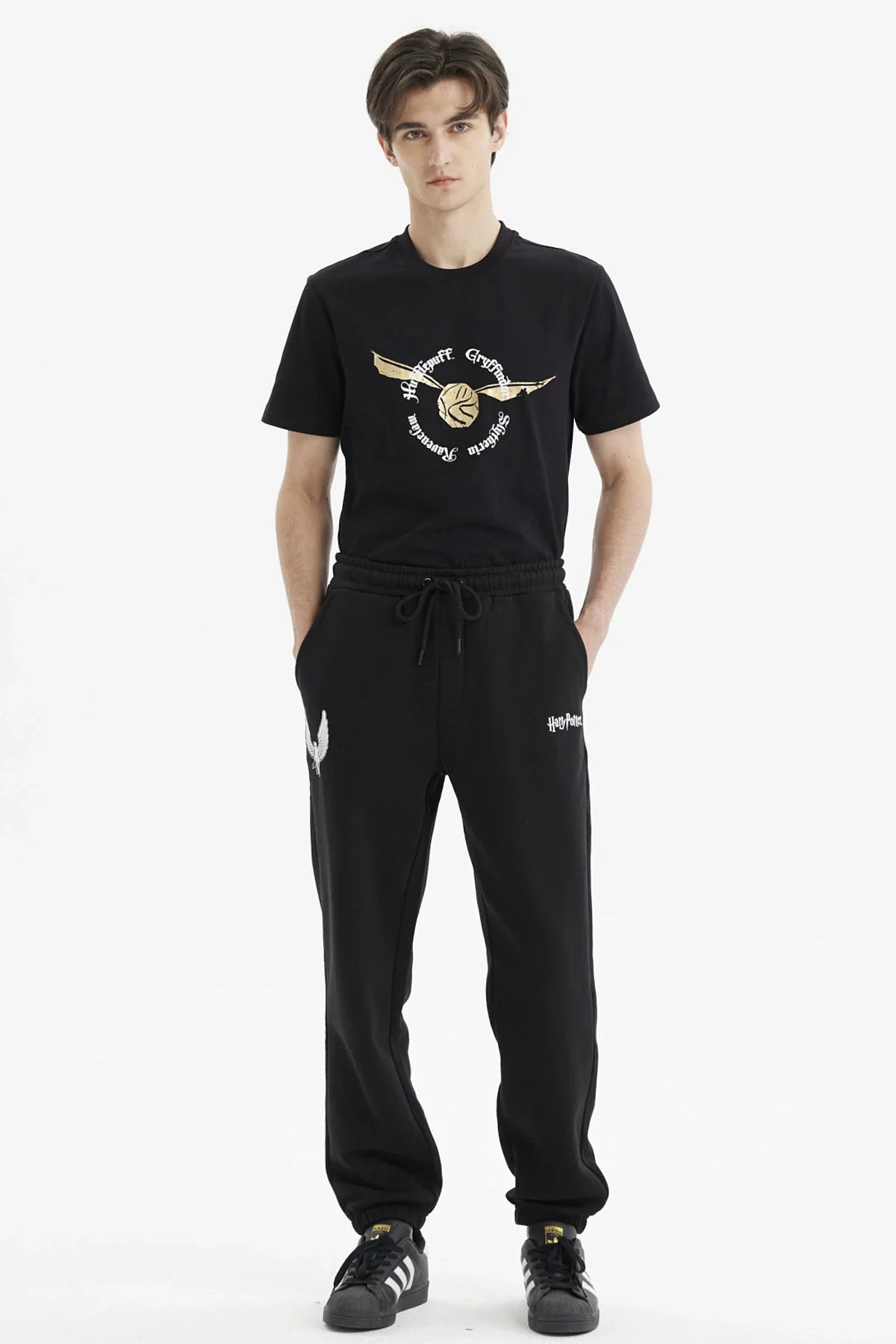 Pantalón buzo negro con el logo de Harry Potter y un estampado de alas plateadas en un costado, ideal para fanáticos de la saga mágica.