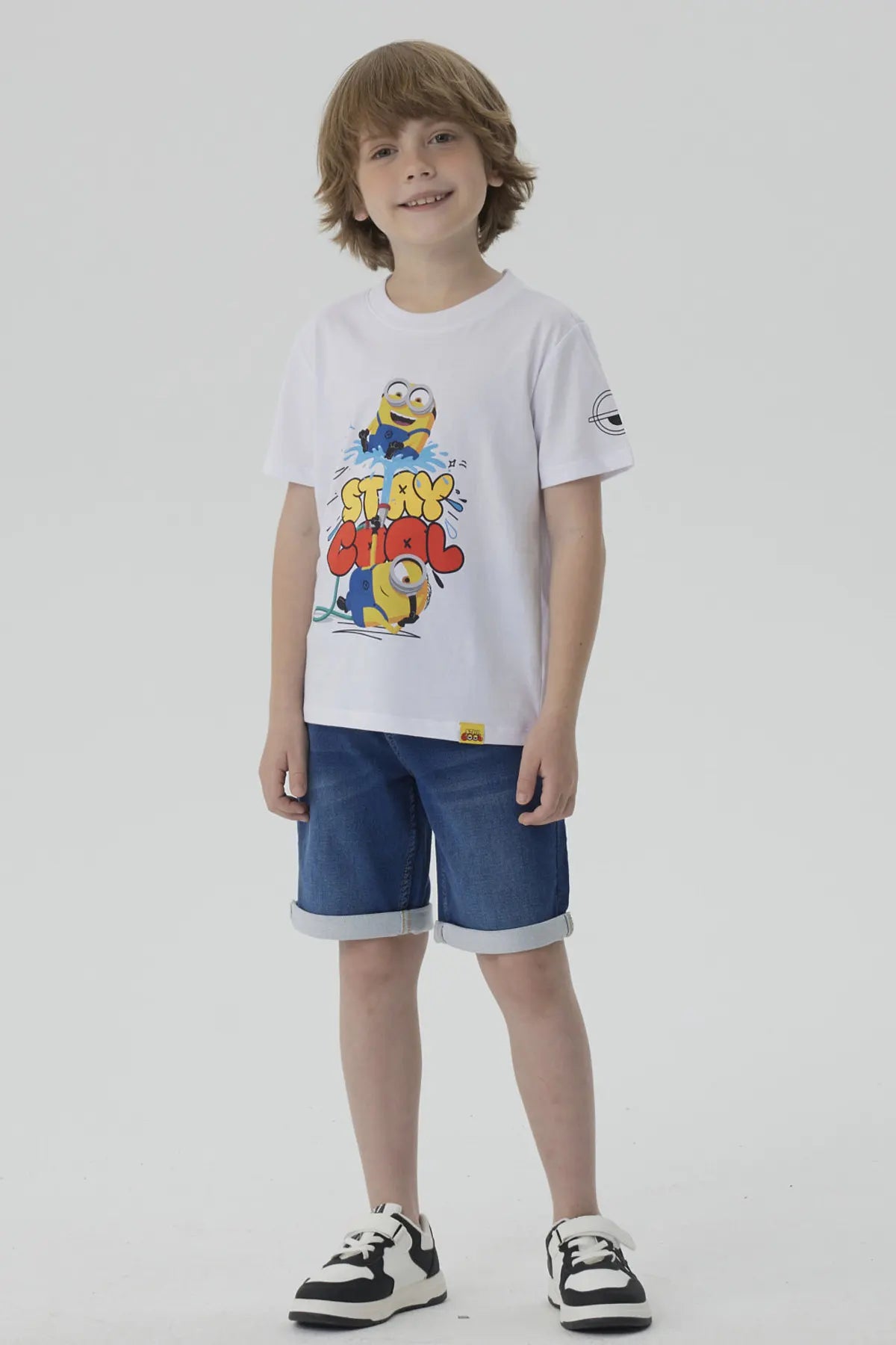 Polera blanca de algodón con estampado de dos Minions jugando y la frase "STAY COOL" en colores vibrantes, ideal para fans de la saga.