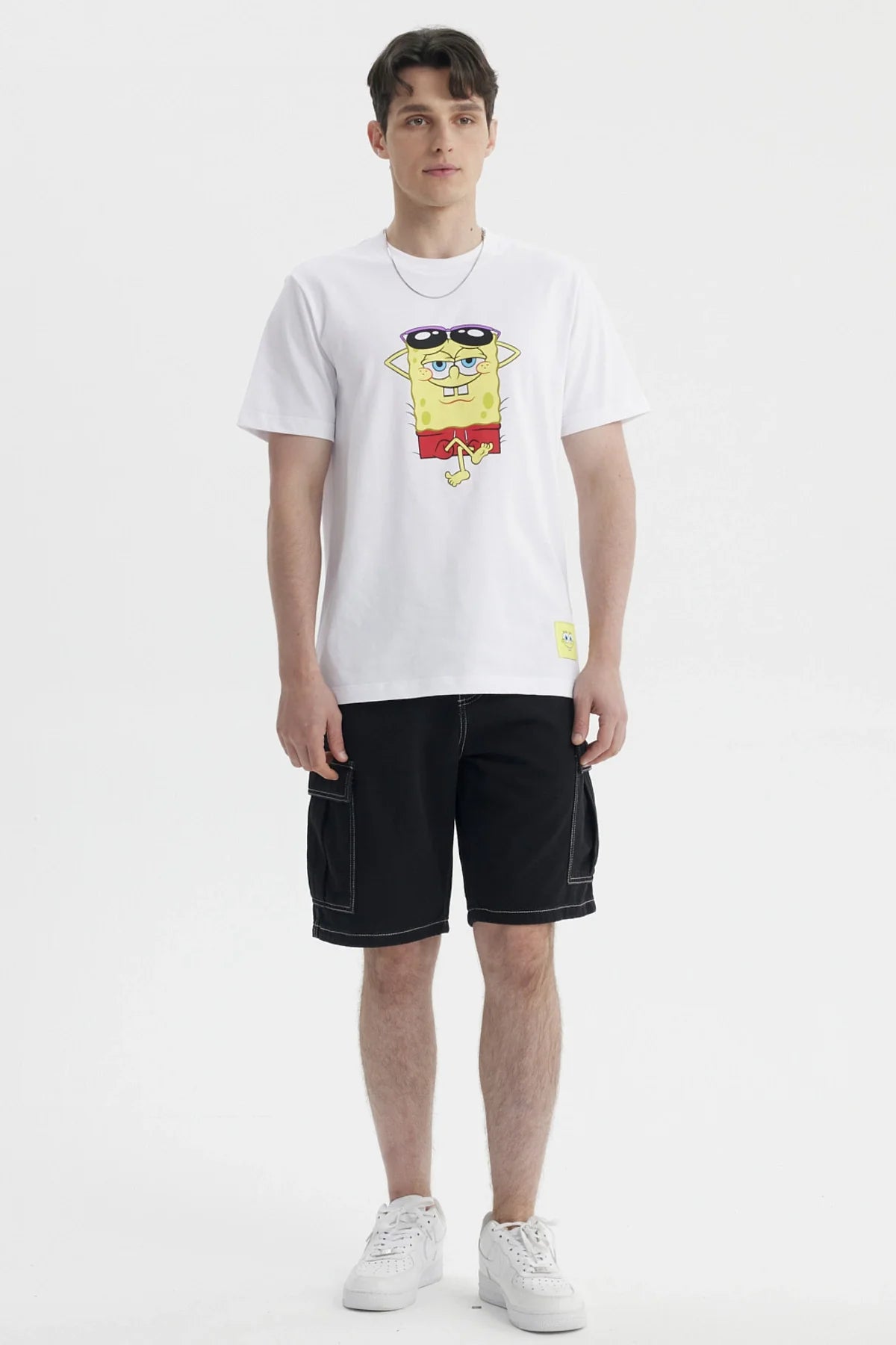 Polera blanca de algodón con un diseño de Bob Esponja relajado usando gafas de sol, capturando su icónica personalidad en un estilo vibrante y divertido.