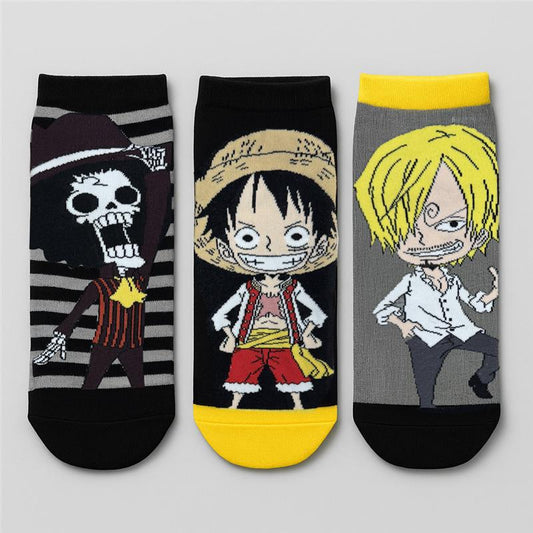 Tripack de calcetas en tonos negros y grises con ilustraciones de personajes icónicos de One Piece: Luffy sonriente, Sanji con su pose desafiante y Brook en su traje de pirata.