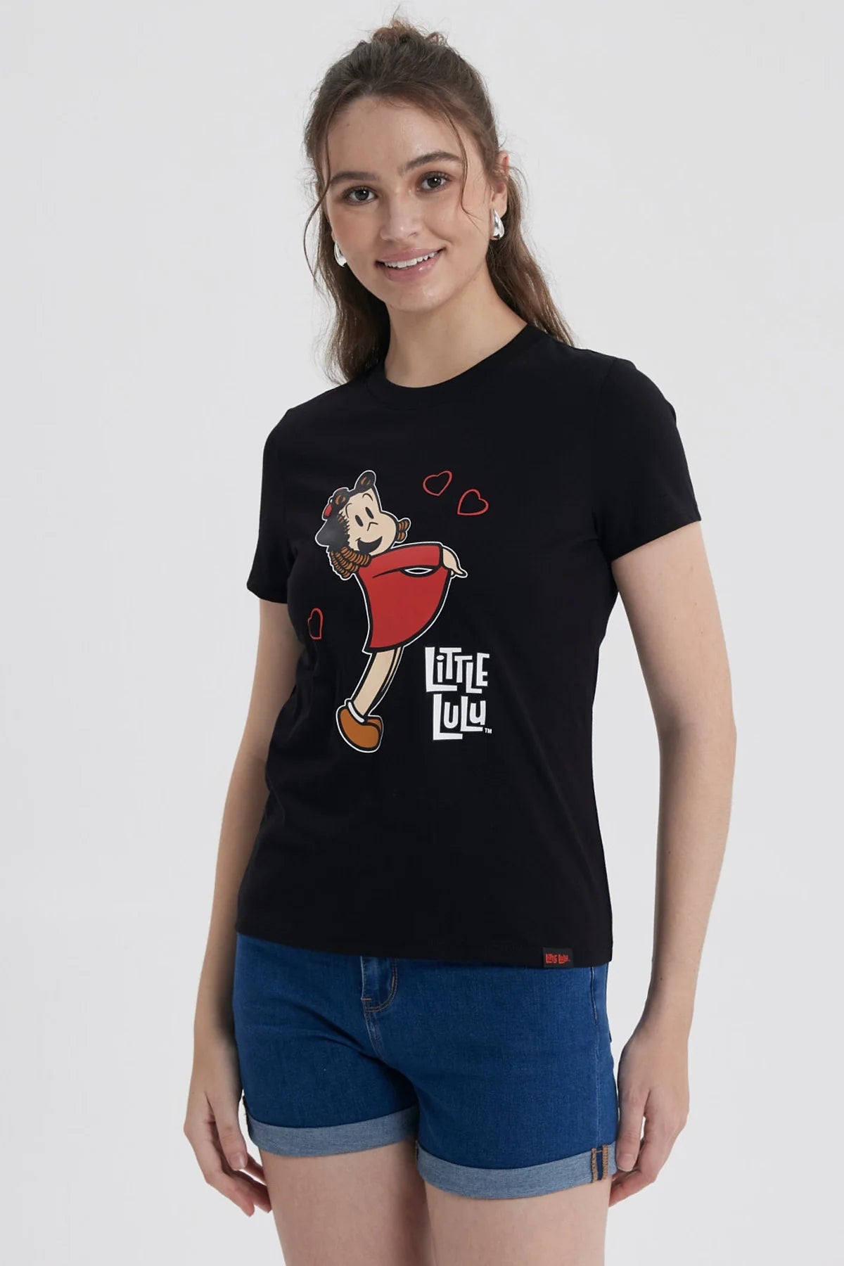 Polera negra de algodón con la icónica ilustración de Pequeña Lulú sonriendo y rodeada de corazones, destacando su vestido rojo y su peinado característico.