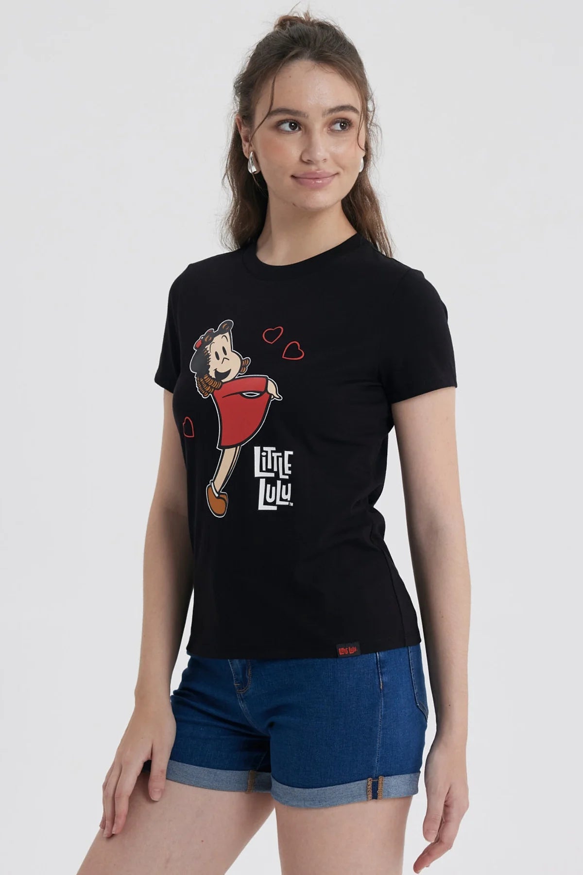 Polera negra de algodón con la icónica ilustración de Pequeña Lulú sonriendo y rodeada de corazones, destacando su vestido rojo y su peinado característico.