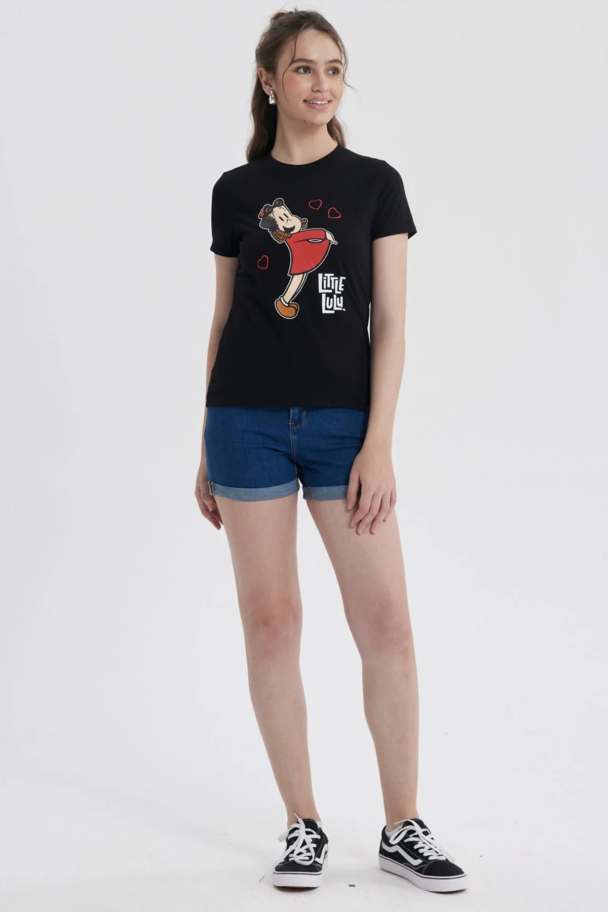 Polera negra de algodón con la icónica ilustración de Pequeña Lulú sonriendo y rodeada de corazones, destacando su vestido rojo y su peinado característico.