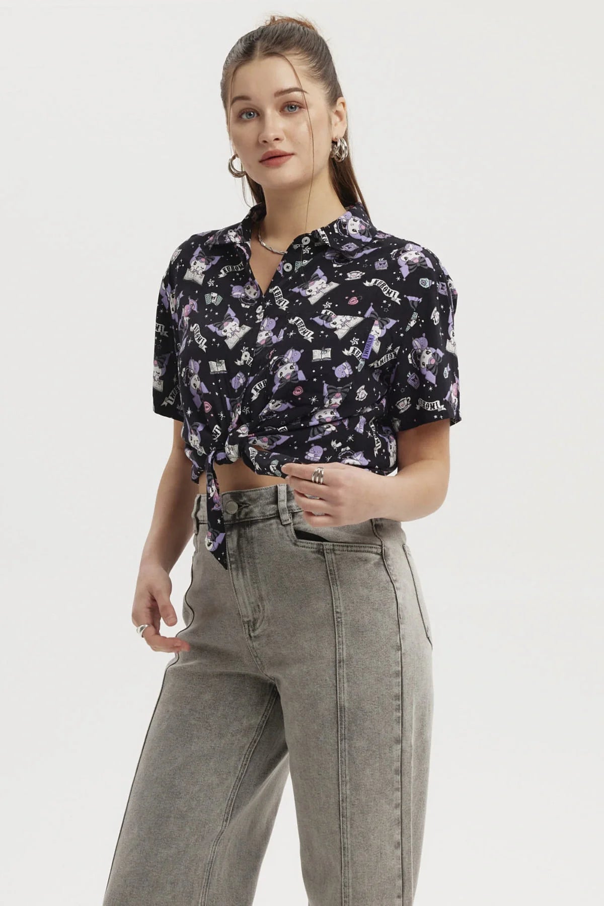 Camisa negra con estampado de Kuromi en tonos morados y blancos, presenta ilustraciones divertidas y detalles de la cultura pop, ideal para fans de Sanrio.