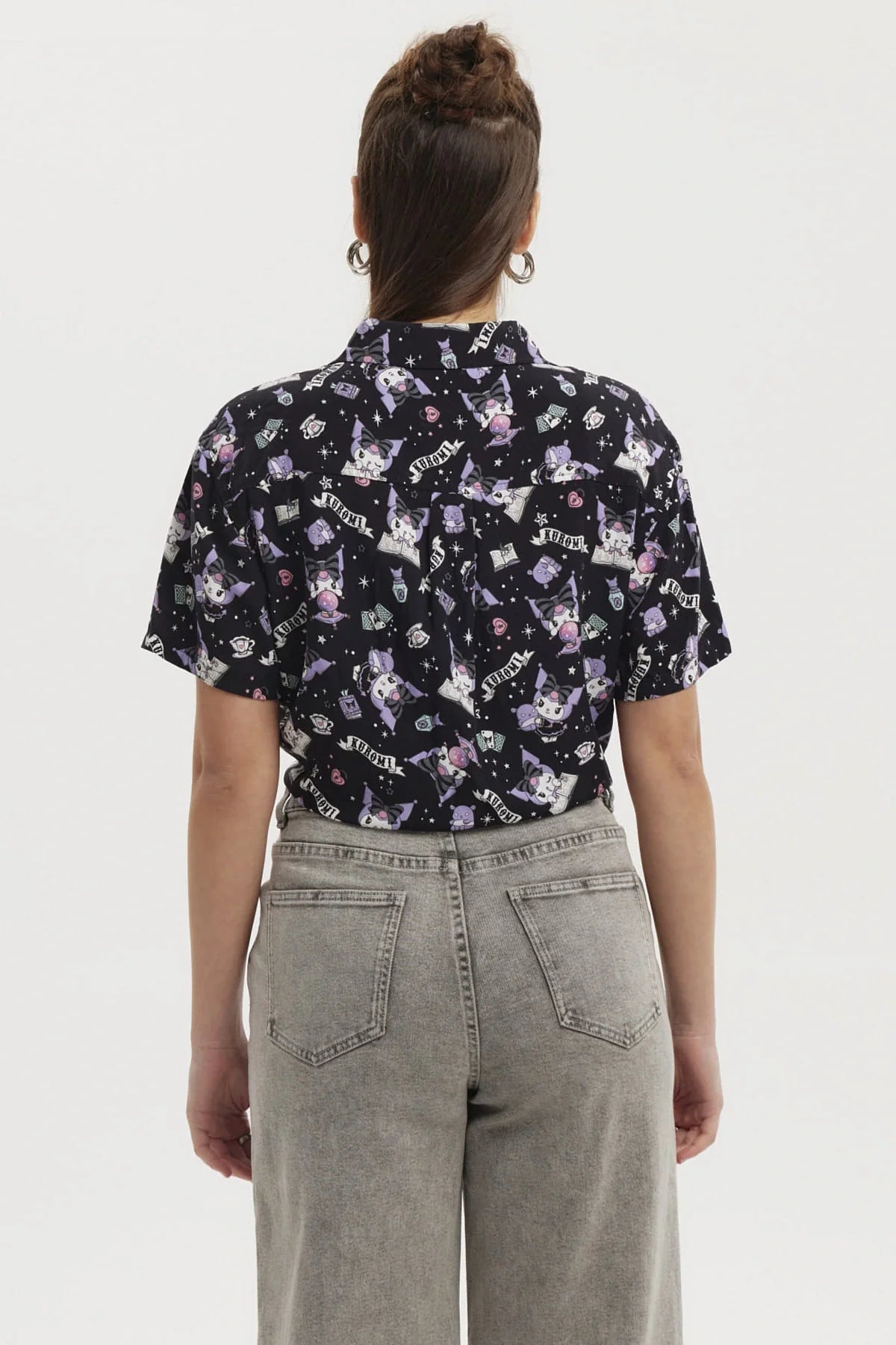 Camisa negra con estampado de Kuromi en tonos morados y blancos, presenta ilustraciones divertidas y detalles de la cultura pop, ideal para fans de Sanrio.