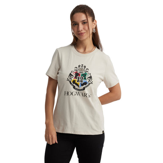 Polera beige de algodón con el escudo de Hogwarts en el centro, colores vibrantes y la palabra 'HOGWARTS' en negro, ideal para fans de Harry Potter.