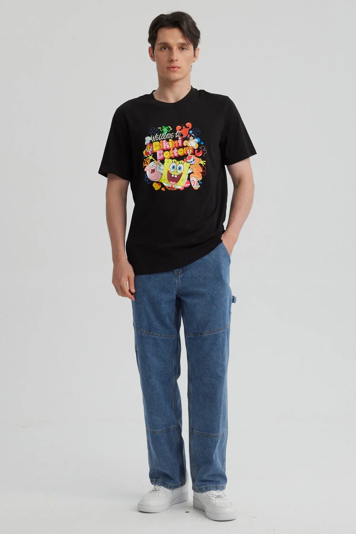 Polera negra de algodón con estampado colorido de Bob Esponja y amigos, mostrando la frase 'Welcome to Bikini Bottom' en un diseño vibrante y divertido.