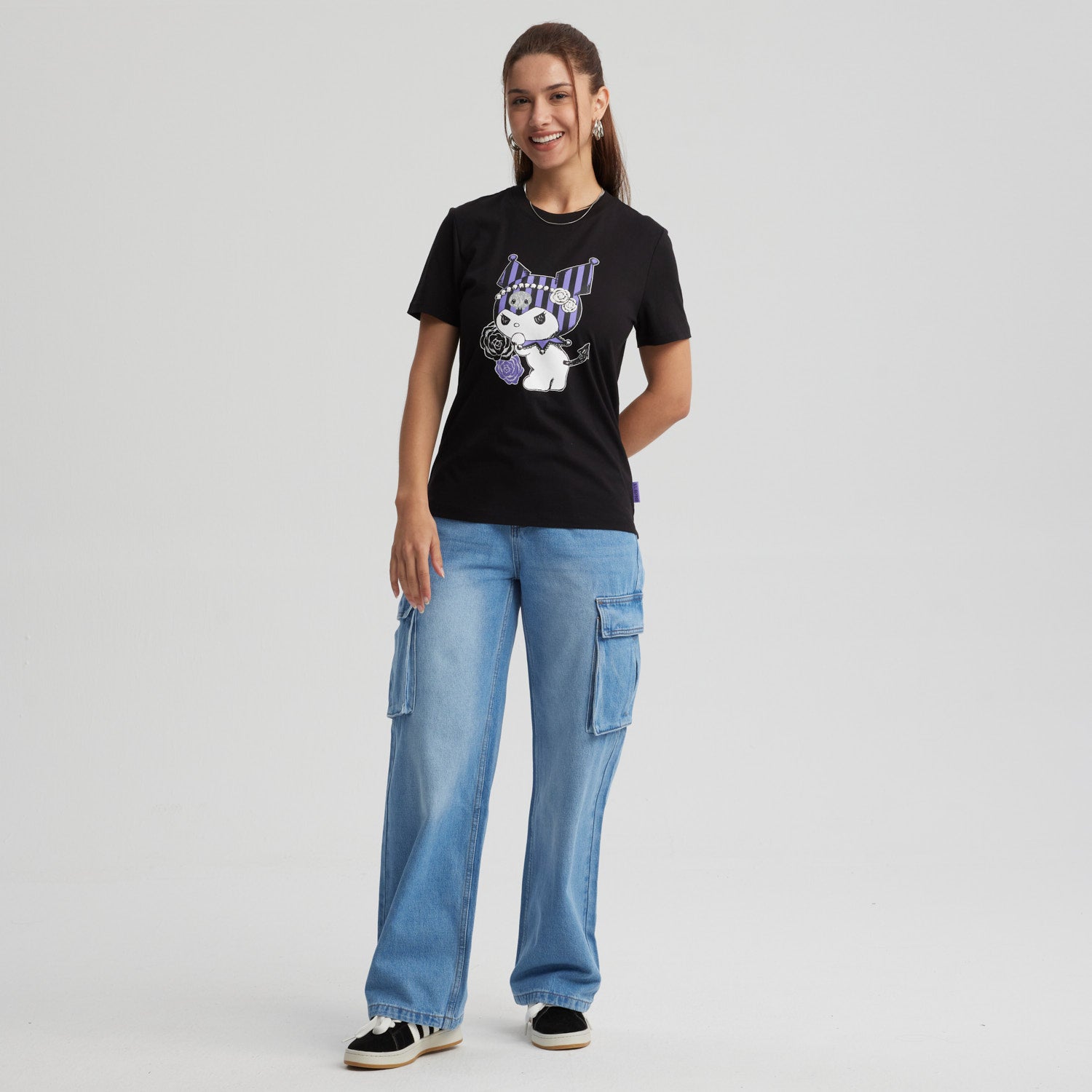 Polera negra de algodón con estampado de Kuromi, un personaje de Sanrio, que sostiene rosas moradas y presenta un diseño de rayas púrpuras en su gorro.