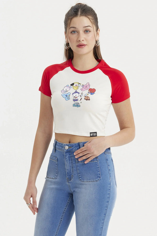Polera crop beige con mangas rojas, presenta un estampado colorido de los personajes BT21 en acción, ideal para fans de BTS y su universo.