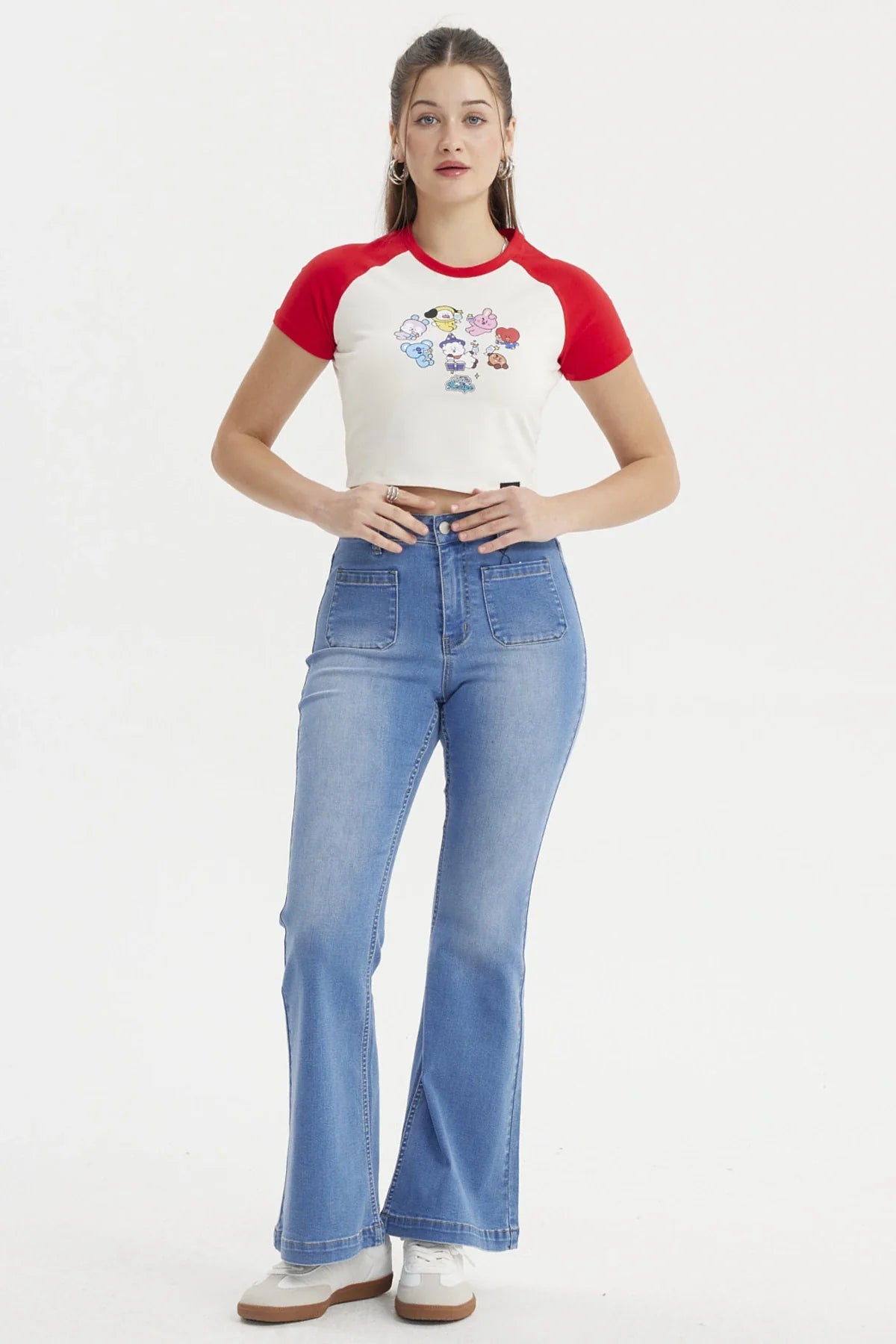 Polera crop beige con mangas rojas, presenta un estampado colorido de los personajes BT21 en acción, ideal para fans de BTS y su universo.