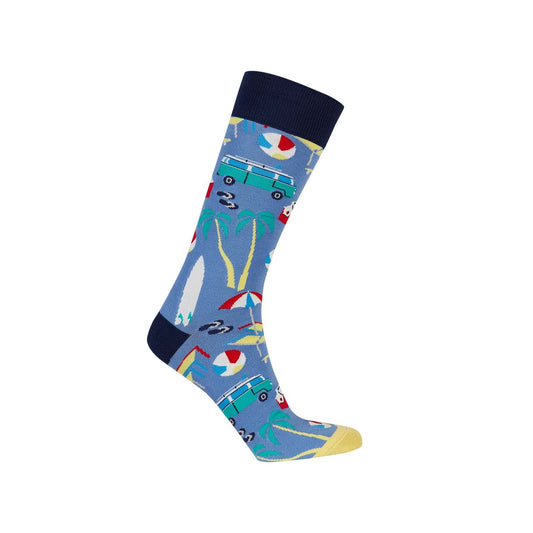 Calcetín de vestir azul claro con estampado veraniego que incluye palmeras, una furgoneta vintage y elementos de playa, ideal para fans de la cultura surf.