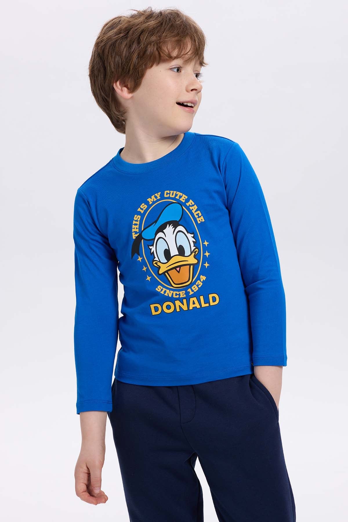 Polera azul con estampado de Pato Donald, diseño gráfico colorido que dice 'THIS IS MY CUTE FACE SINCE 1934' en un estilo divertido y juvenil.