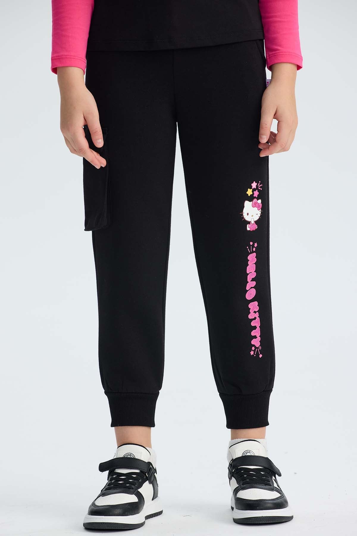 Pantalón buzo cargo negro con estampado de Hello Kitty en tonos rosa y amarillo, mostrando a la icónica gatita con su moño, ideal para fans de Sanrio.
