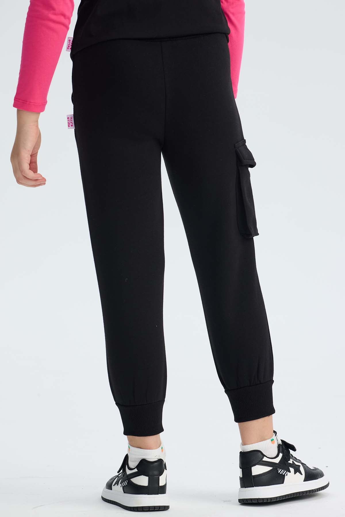 Pantalón buzo cargo negro con estampado de Hello Kitty en tonos rosa y amarillo, mostrando a la icónica gatita con su moño, ideal para fans de Sanrio.