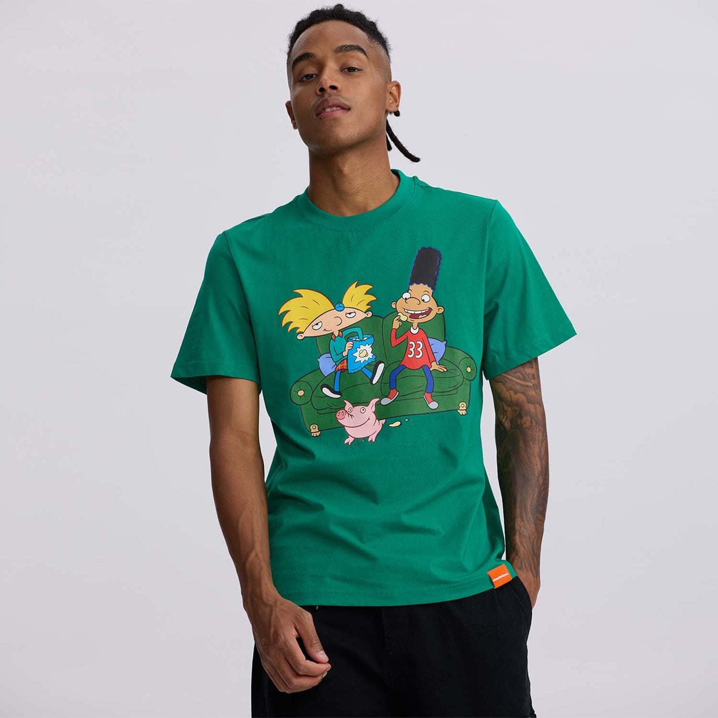 Polera verde de algodón con ilustración de Arnold, Gerald y Helga en un sofá, evocando la nostalgia de 'Hey Arnold' con colores vibrantes y detalles icónicos.
