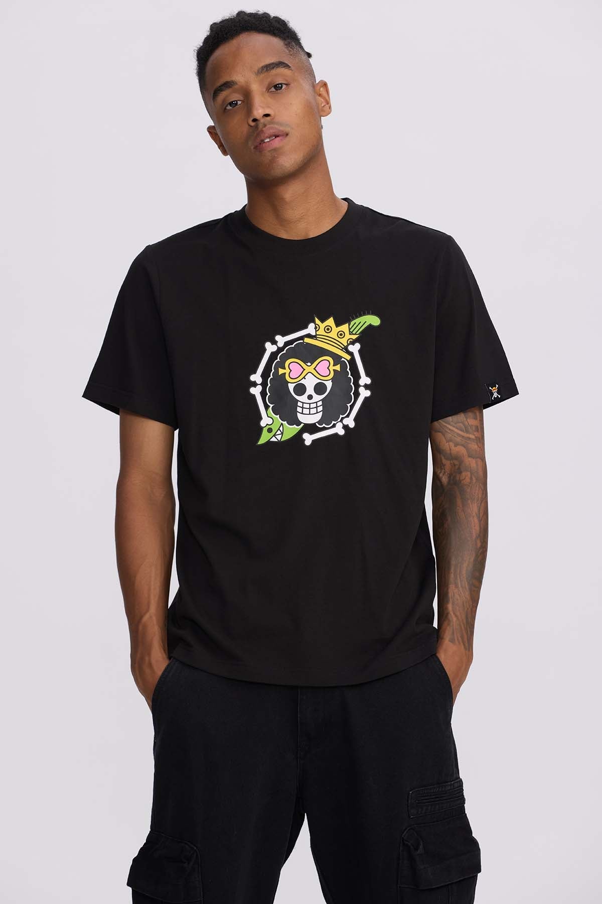 Polera negra de algodón con ilustración colorida de Brook, el esqueleto músico de One Piece, destacando su corona y gafas rosas en un diseño vibrante.