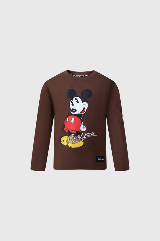 Polera de algodón color café con ilustración de Mickey Mouse sonriendo y sosteniendo su pantalón rojo, diseño icónico que celebra la esencia del universo Disney.