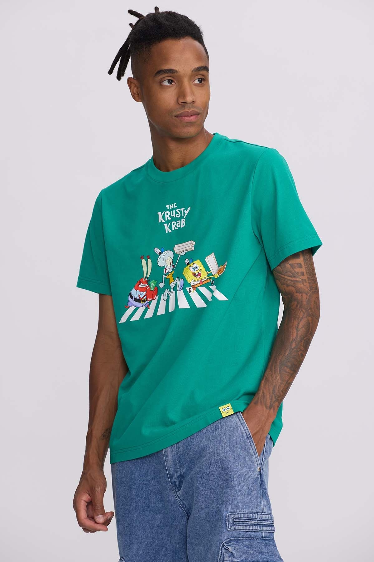 Polera verde con estampado de los personajes Bob Esponja, Calamardo y Don Cangrejo en la famosa escena de cruce peatonal, representando el Krusty Krab.