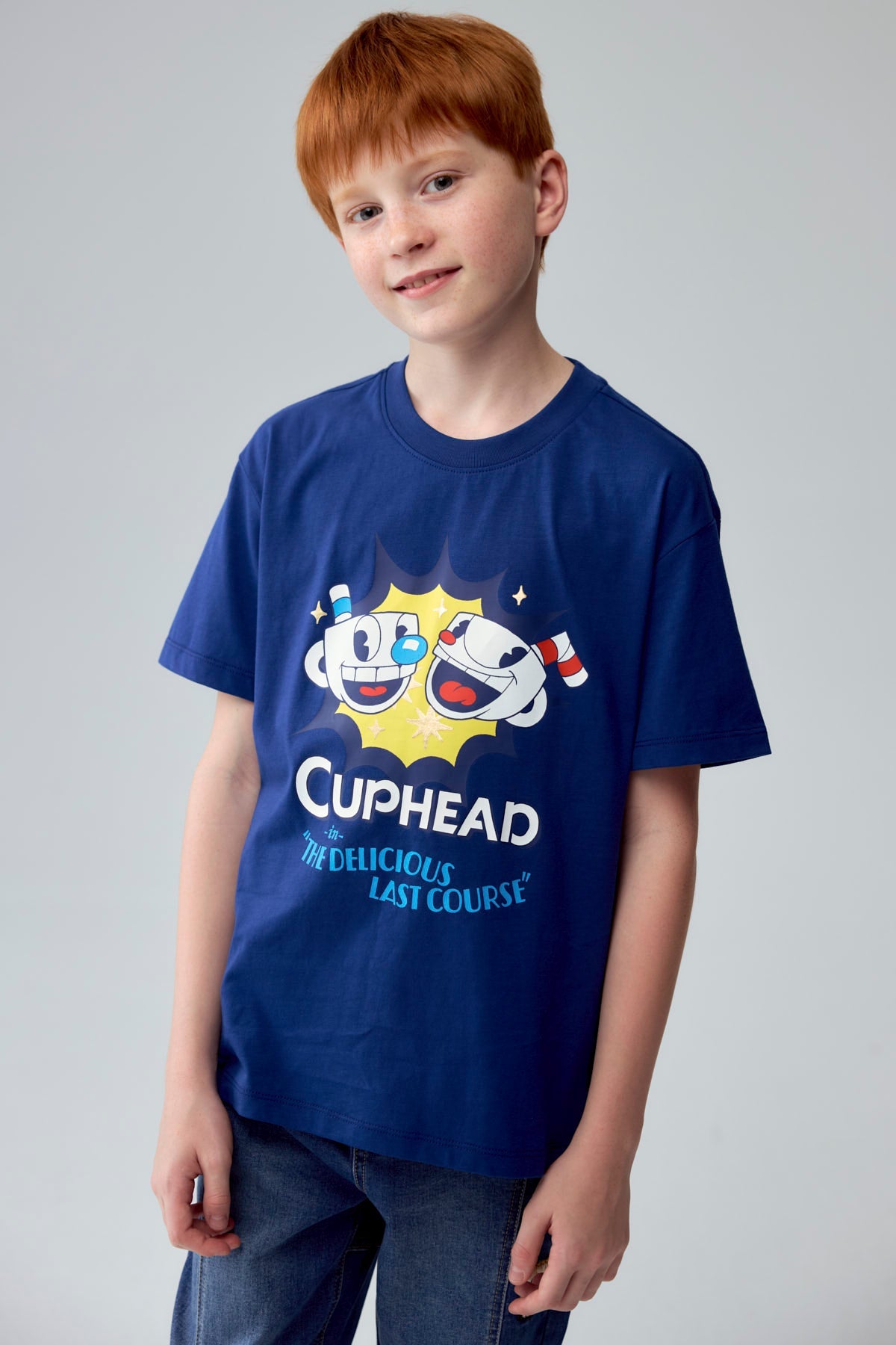 Polera azul de Cuphead con ilustración vibrante de Cuphead y Mugman sonriendo, destacando el título 'Cuphead in The Delicious Last Course' en un diseño retro.