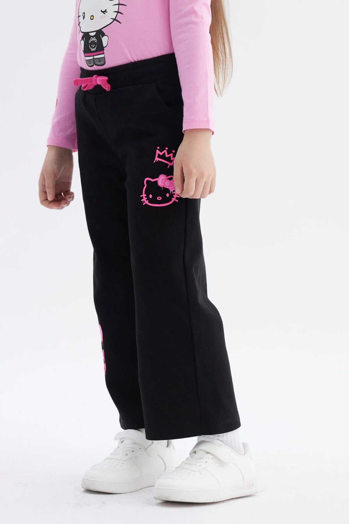 Pantalón buzo negro con detalles en rosa, presenta ilustraciones de Hello Kitty en estilo moderno, ideal para fans de la cultura pop y el kawaii.
