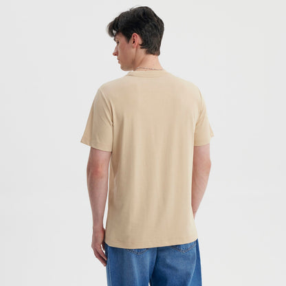 Polera beige de algodón con el escudo de Hogwarts en colores vibrantes, destacando los cuatro emblemas de las casas y la letra H, ideal para fans de Harry Potter.