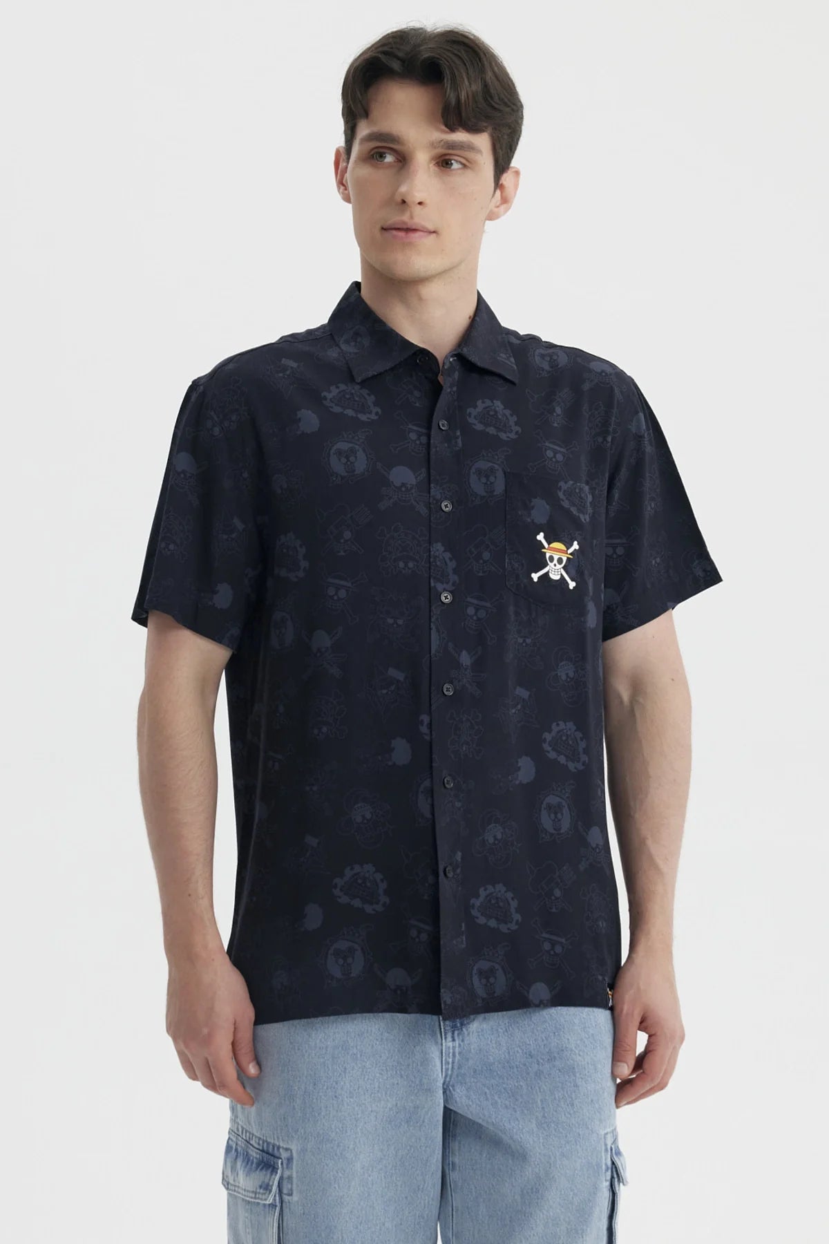 Camisa de manga corta negra con estampado sutil de personajes de One Piece, incluye el icónico logo de la tripulación de Luffy en el pecho.