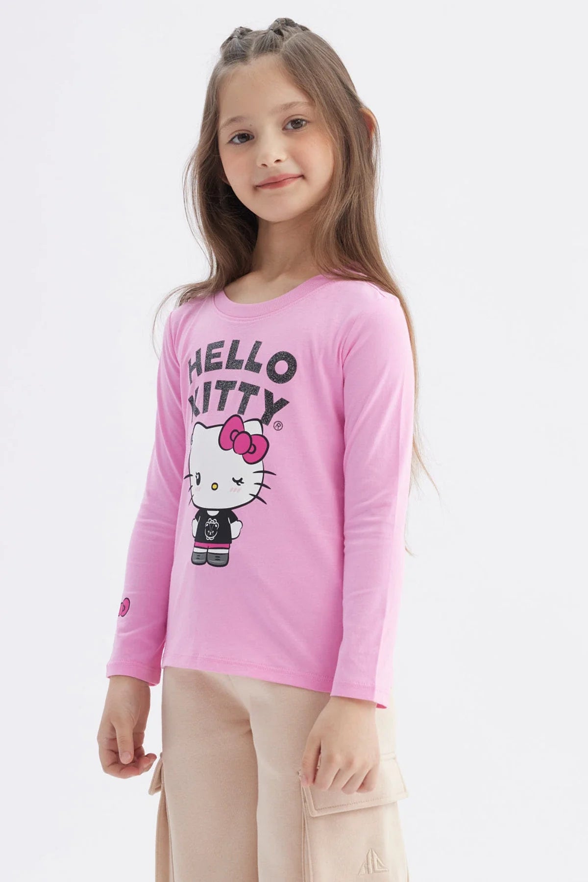 Polera de manga larga en color rosado con un diseño central de Hello Kitty vistiendo un conjunto negro, acompañado del texto 'HELLO KITTY' en letras brillantes.