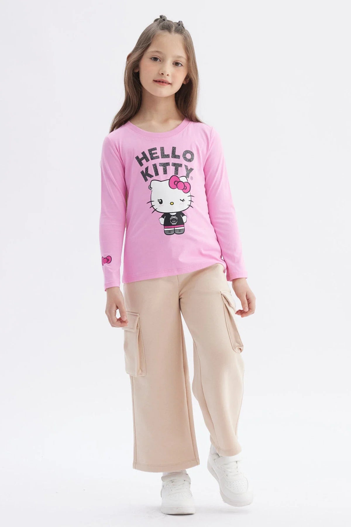 Polera de manga larga en color rosado con un diseño central de Hello Kitty vistiendo un conjunto negro, acompañado del texto 'HELLO KITTY' en letras brillantes.