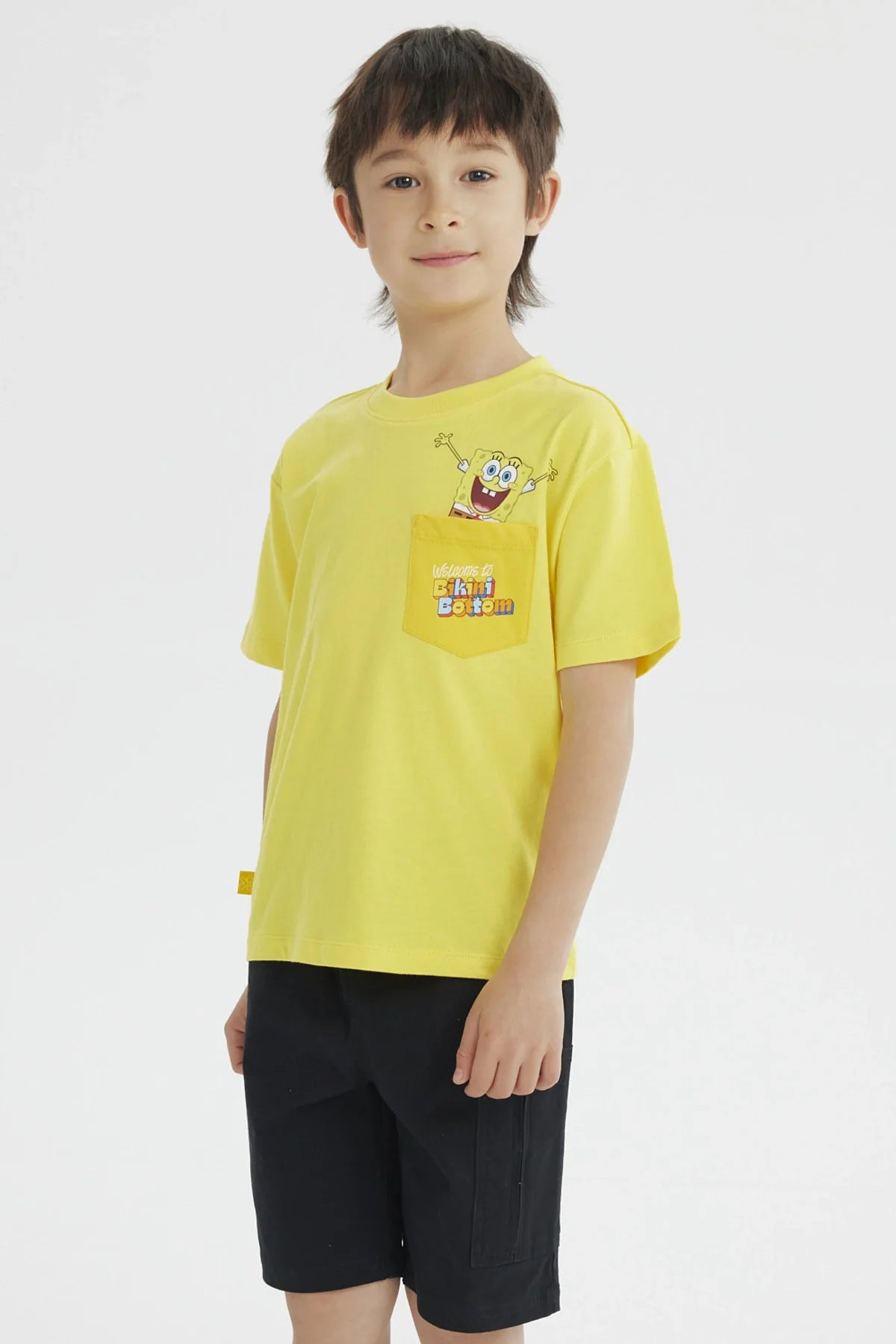 Polera amarilla de algodón con un divertido diseño de Bob Esponja en el bolsillo, que dice 'Welcome to Bikini Bottom', ideal para fans de la serie.