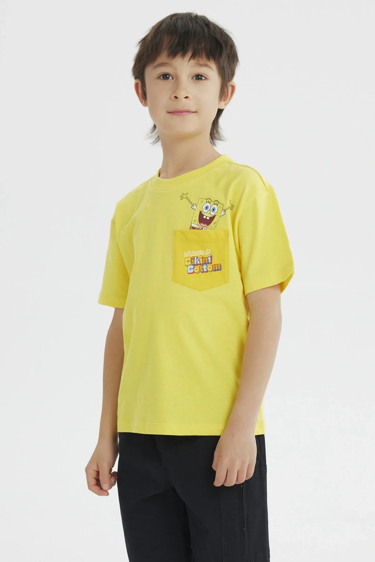 Polera amarilla de algodón con un divertido diseño de Bob Esponja en el bolsillo, que dice 'Welcome to Bikini Bottom', ideal para fans de la serie.