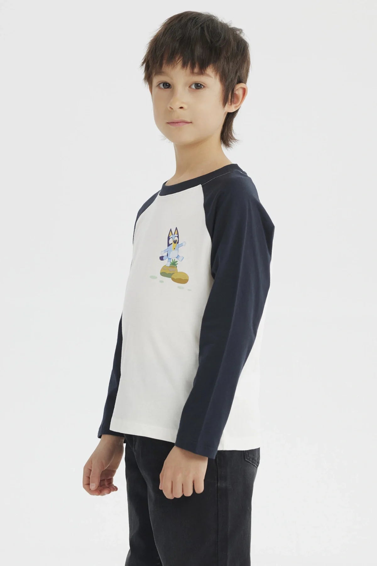Polera de manga larga azul marino con cuerpo blanco, presenta a Bluey en acción sobre un fondo de colores suaves, ideal para fans de la serie australiana.