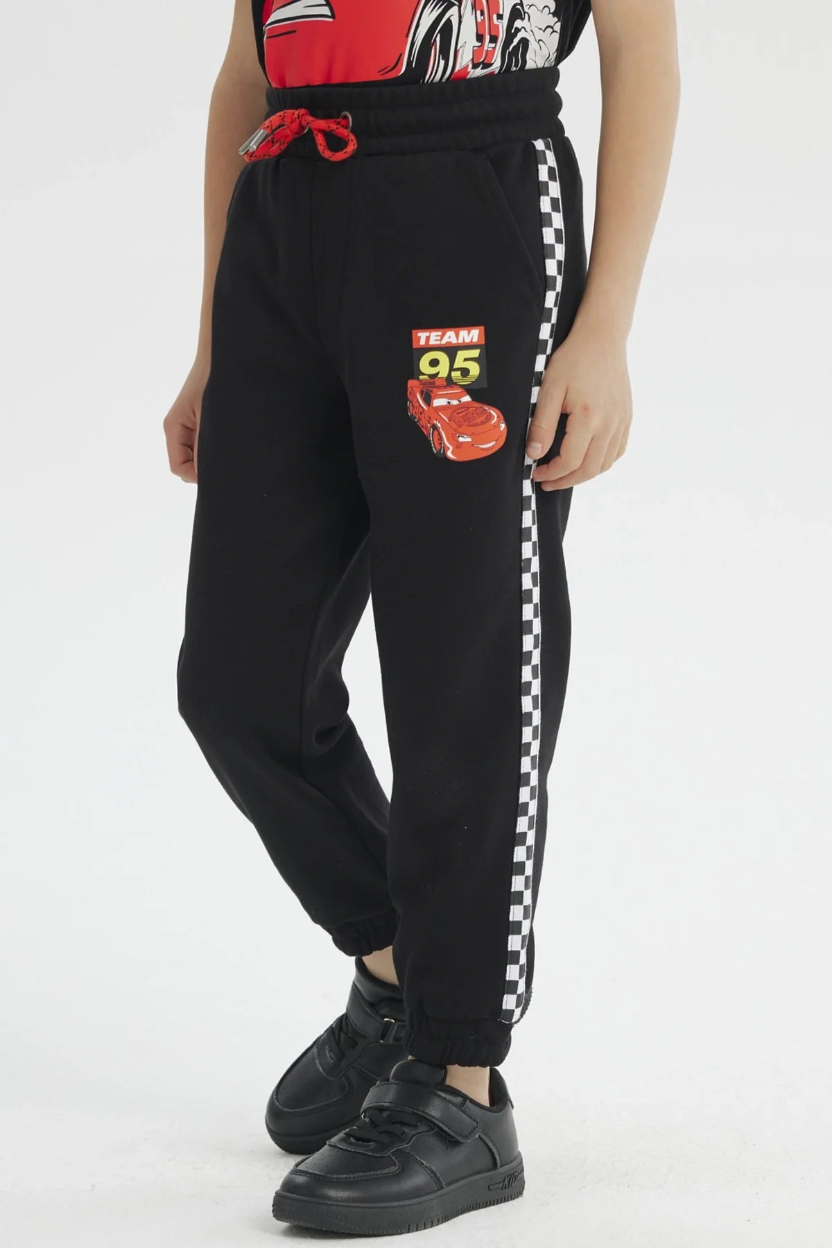 Pantalón buzo negro con detalles de 'Team 95' y un diseño vibrante de Rayo McQueen, ideal para los fans de Cars, con bandas a cuadros en los laterales.