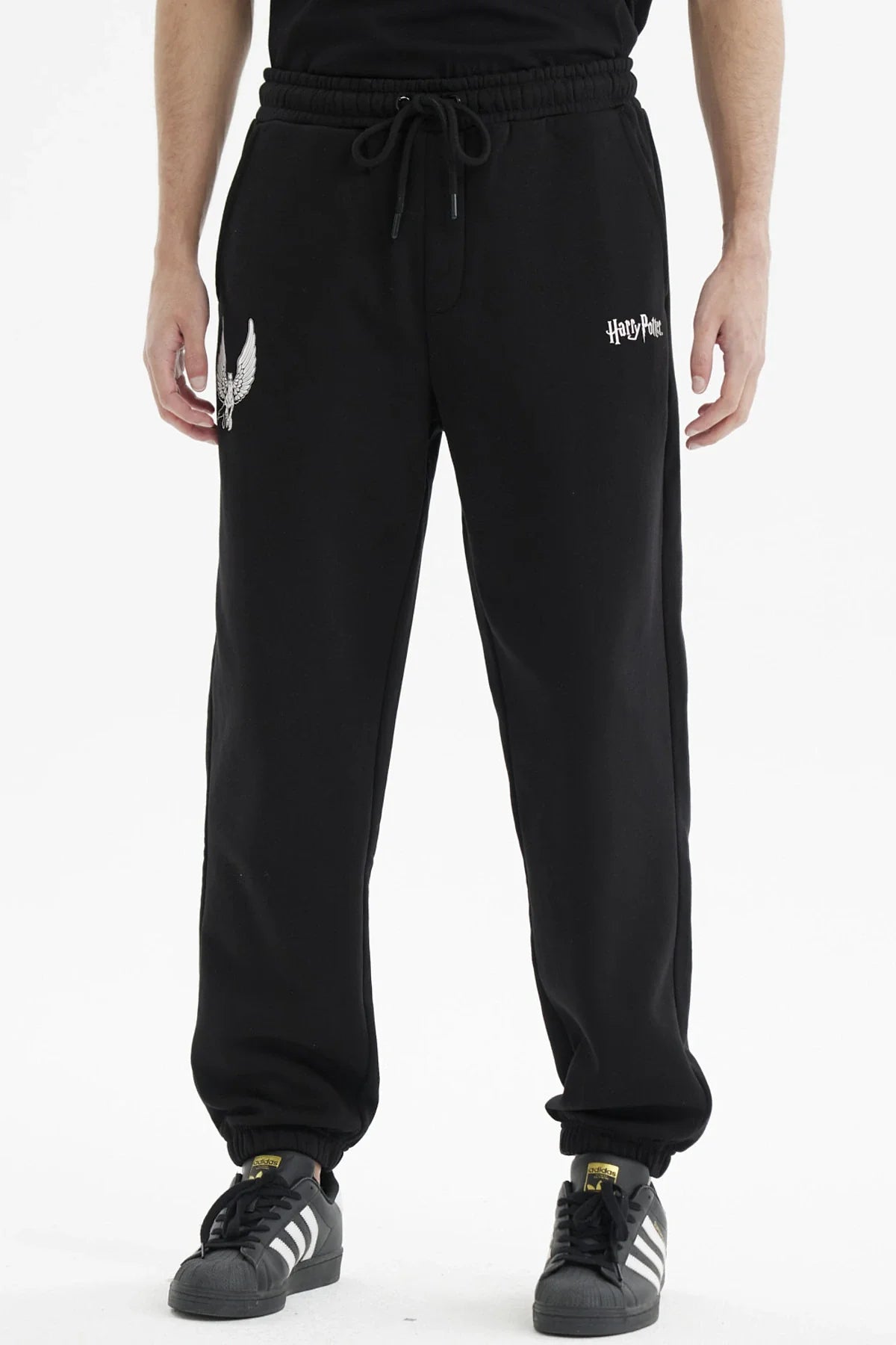 Pantalón buzo negro con el logo de Harry Potter y un estampado de alas plateadas en un costado, ideal para fanáticos de la saga mágica.