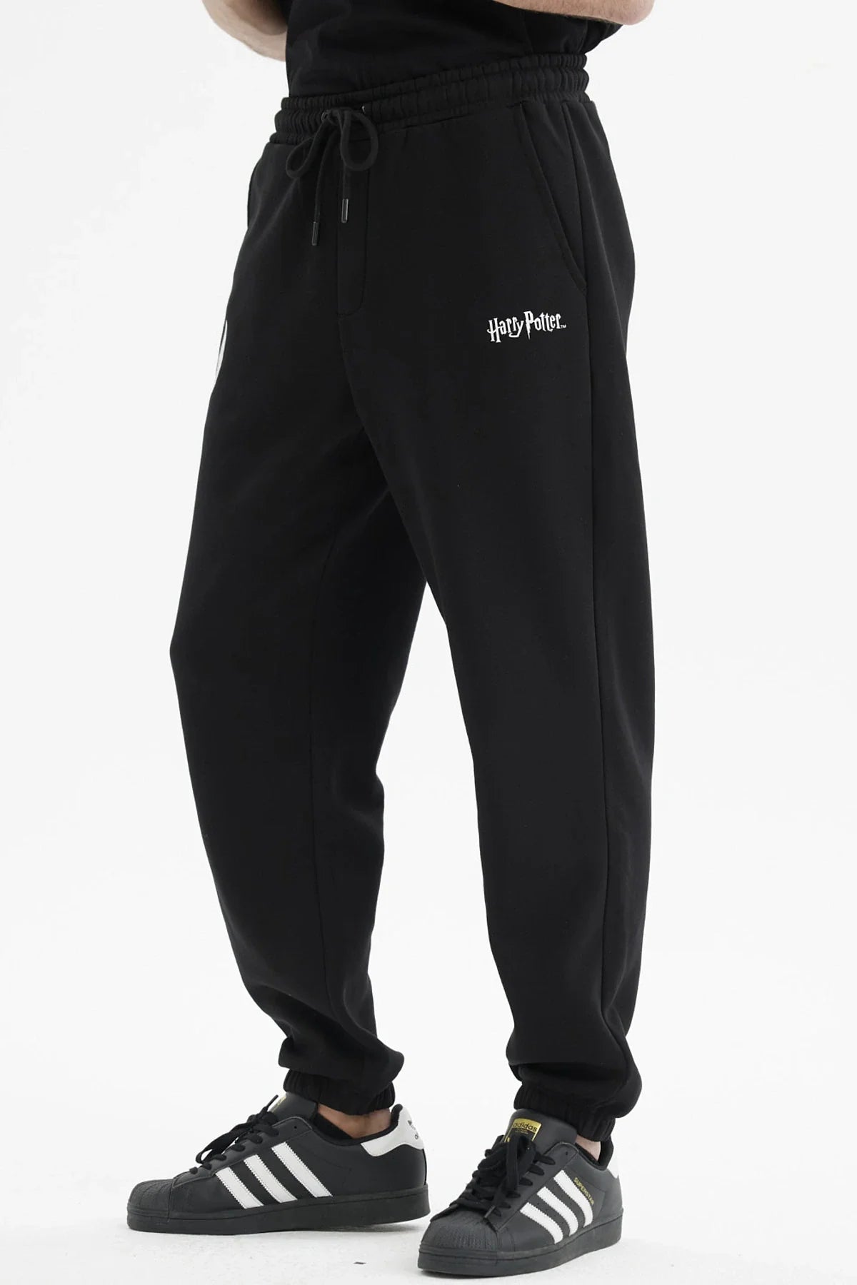Pantalón buzo negro con el logo de Harry Potter y un estampado de alas plateadas en un costado, ideal para fanáticos de la saga mágica.