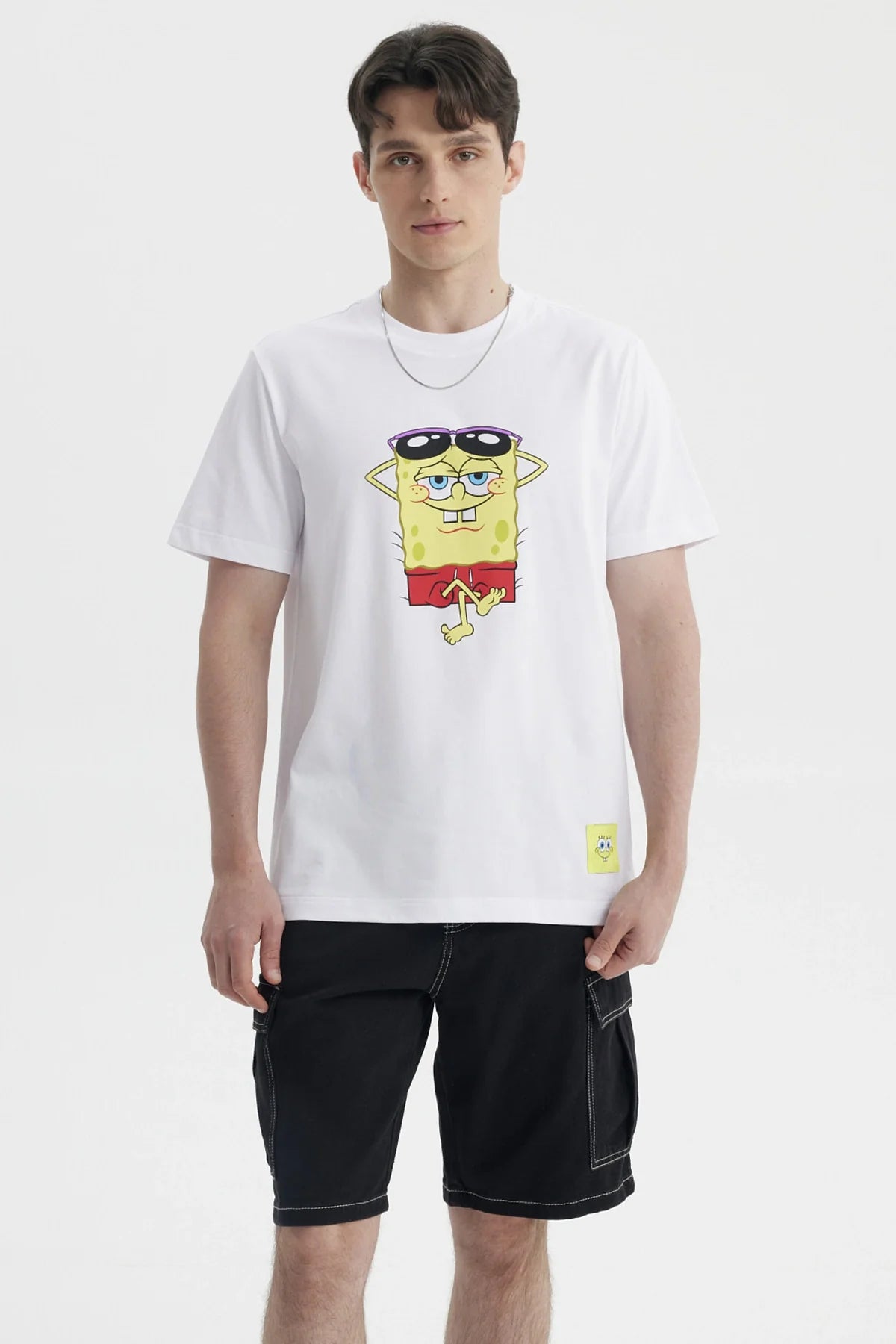 Polera blanca de algodón con un diseño de Bob Esponja relajado usando gafas de sol, capturando su icónica personalidad en un estilo vibrante y divertido.
