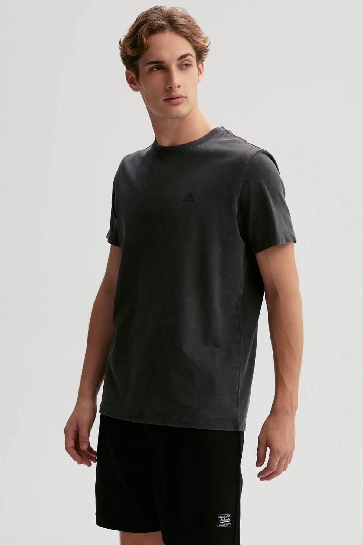 Polera negra de algodón 100% con diseño minimalista de logo en el pecho, ideal para los fanáticos de la moda urbana y el estilo casual.