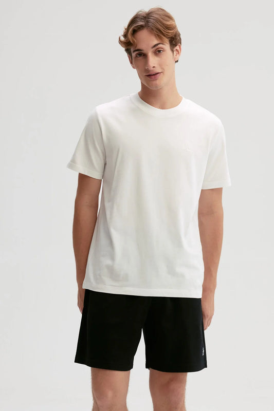 Polera blanca de algodón con diseño minimalista, presenta un logo sutil en el pecho, ideal para fans de la moda casual y contemporánea.